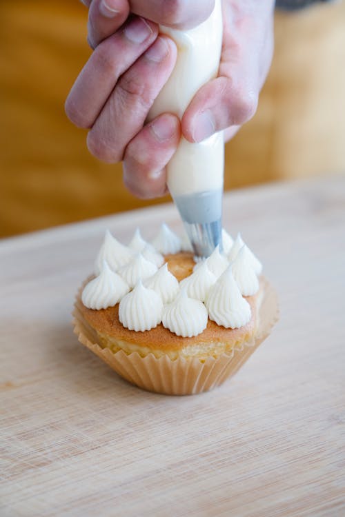 Person Putting Whipped Cream on Cupcake