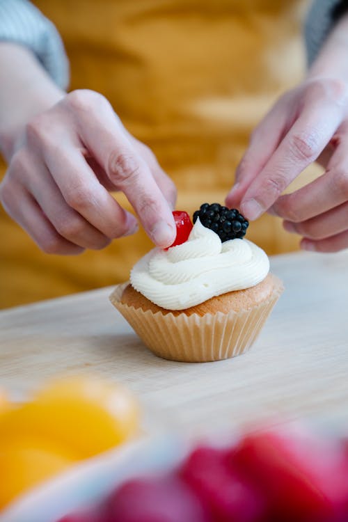 Person Putting Toppings on a Cupcake