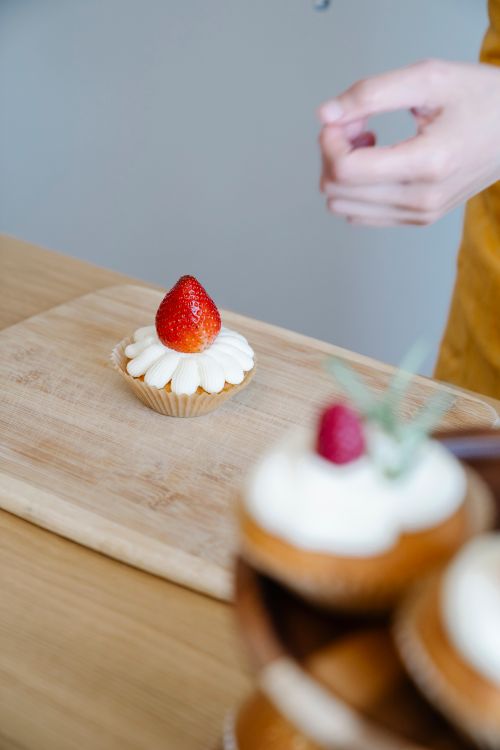 Free Delicious strawberry topped cupcake on a wooden board, perfect for dessert lovers. Stock Photo