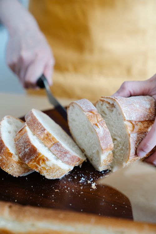 Free Close-up of hands slicing fresh artisan bread on a wooden board, showcasing texture. Stock Photo