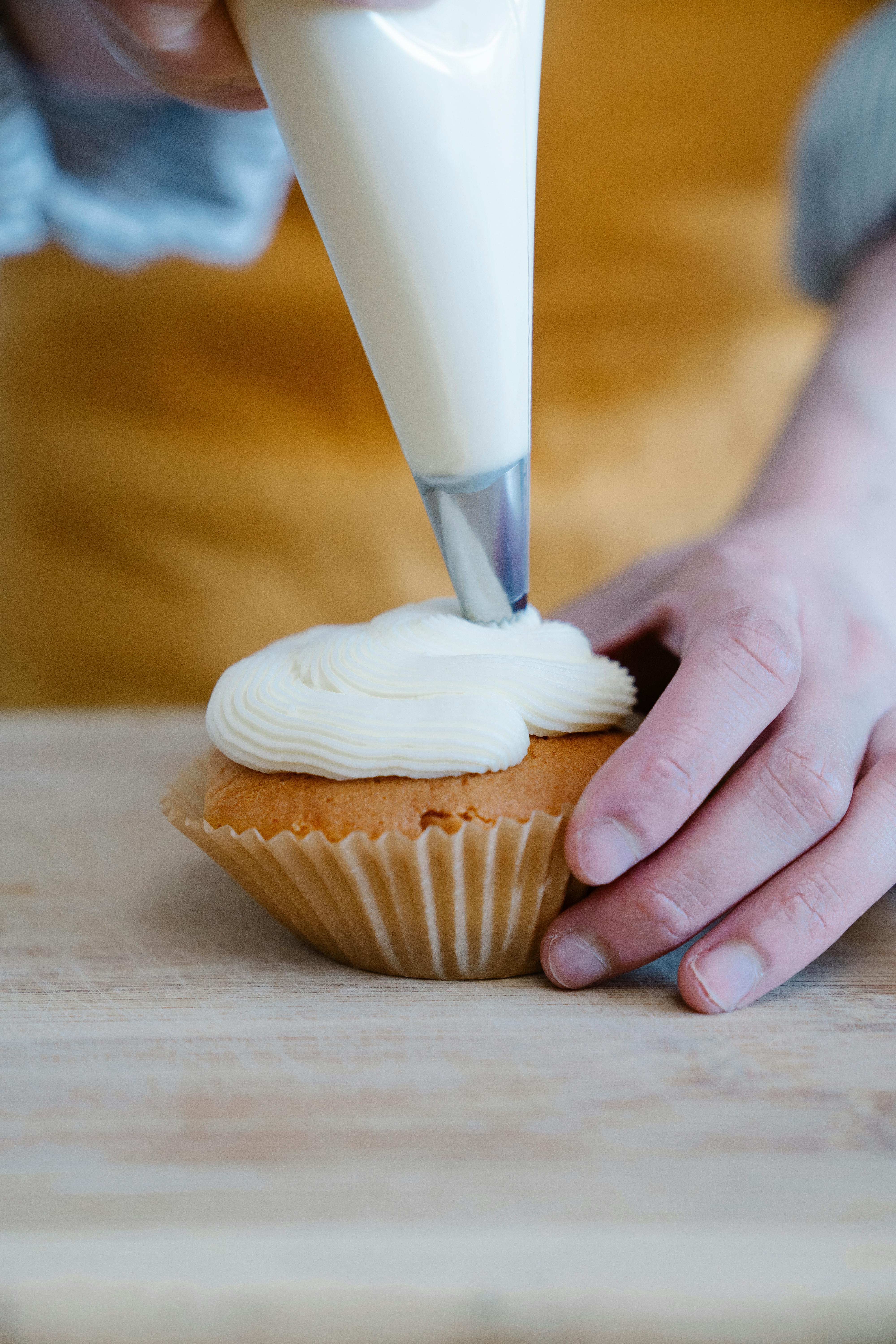 person decorating a cupcake