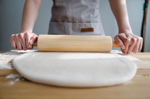 Free Close-up of hands using a rolling pin to prepare dough on a wooden kitchen surface. Stock Photo