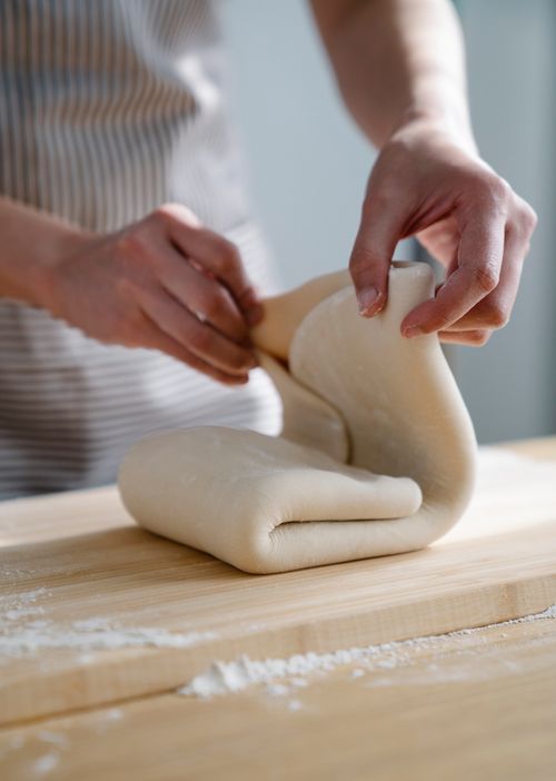 Free A woman skillfully folds dough on a floured surface in a bright kitchen, preparing for baking. Stock Photo