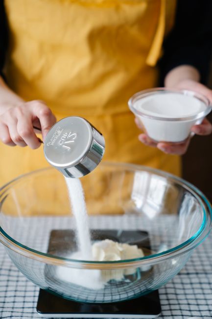 Nested stainless steel measuring cups filled with flour, granulated sugar, and softened butter arranged next to a digital kitchen scale displaying a gram weight.