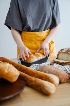 Baker in yellow apron handling freshly baked artisan breads in a kitchen setting.