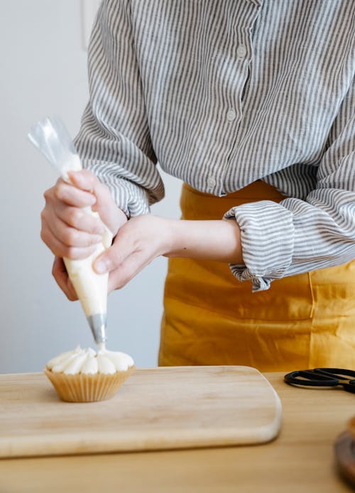 Person Putting Whipped Cream on a Cupcake