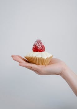 Close-up of a cupcake topped with a strawberry, held in a hand.