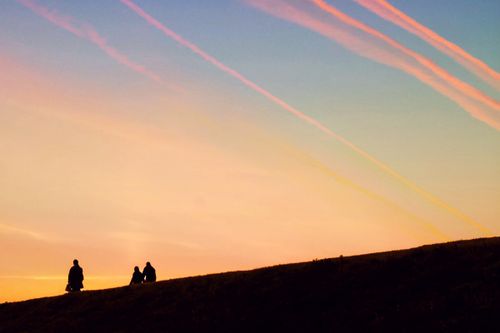 Free Two people silhouetted against a vibrant sunset sky with streaking contrails. Stock Photo