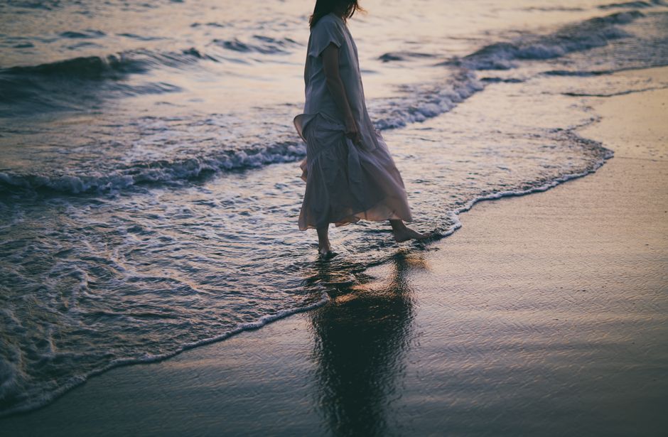 Serene view of a woman in a dress walking barefoot by the waves at sunset.
