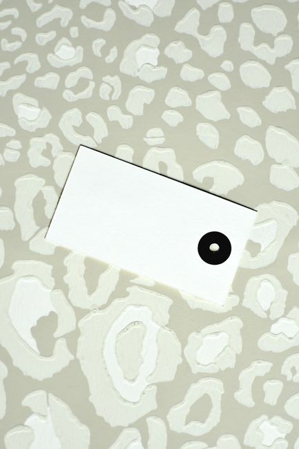A white card with a black dot on a textured abstract pattern surface.