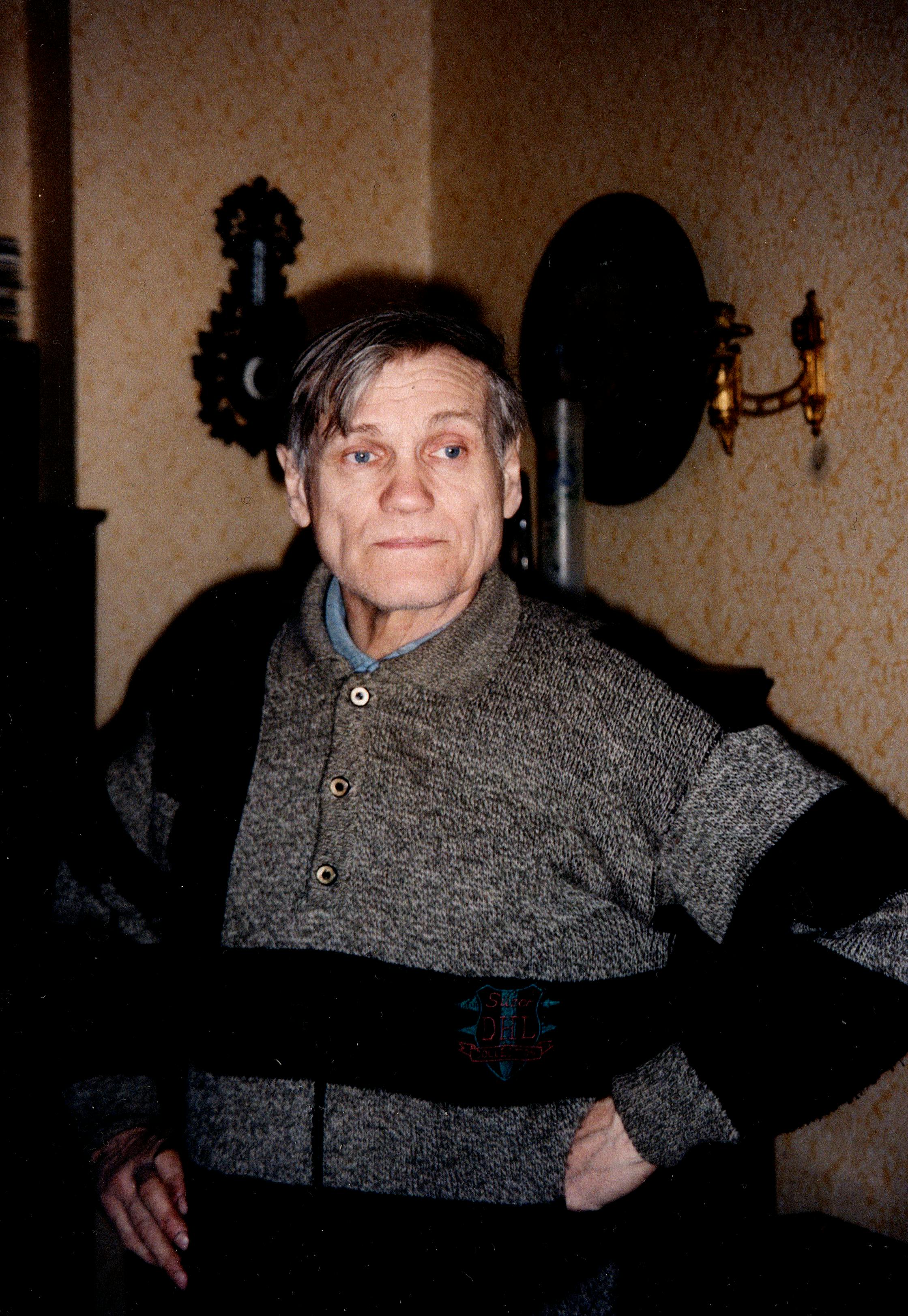 Senior adult man in a sweater standing indoors with decorative wall elements.