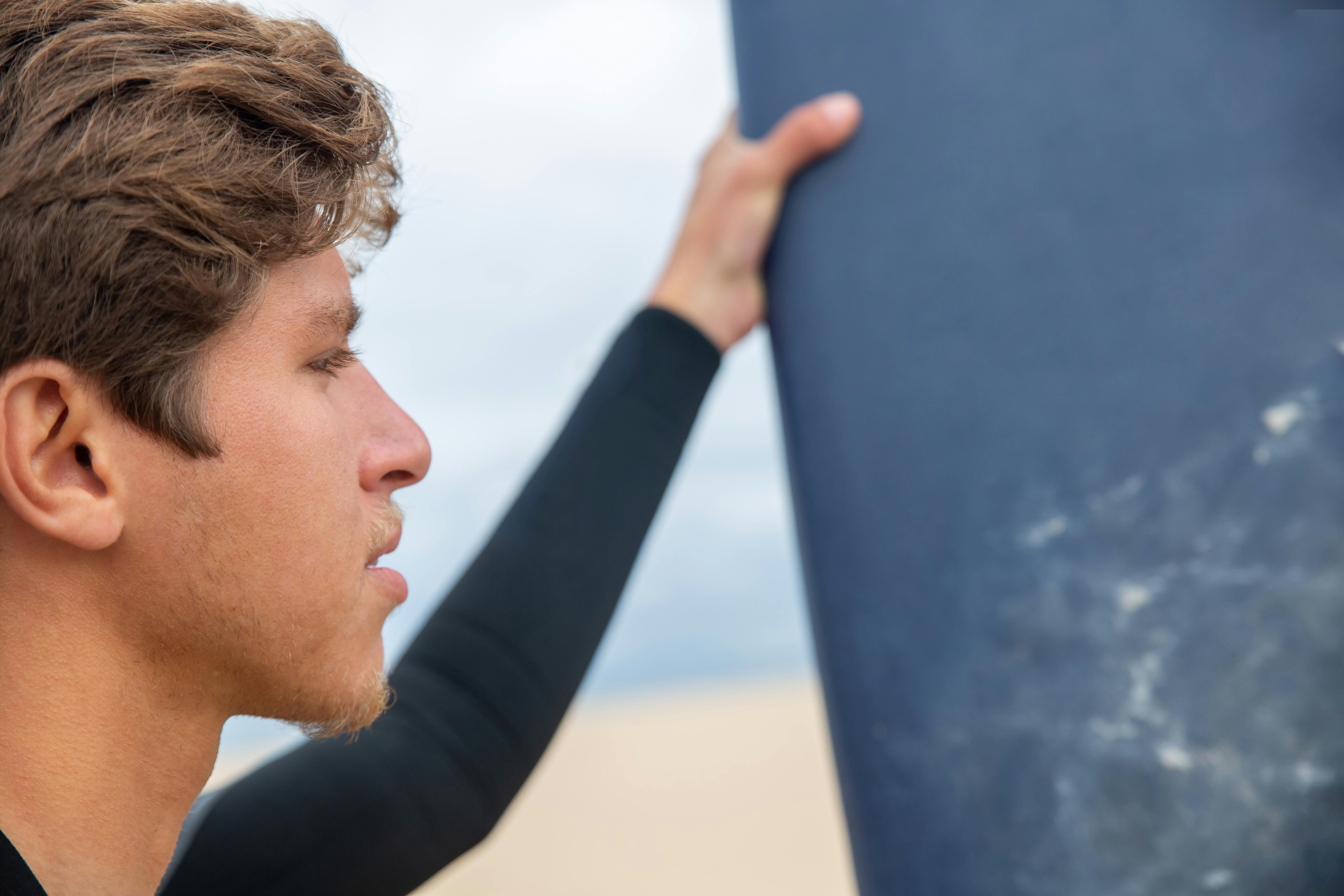 Side view of a man holding a surfboard at the beach, showcasing surfing lifestyle.