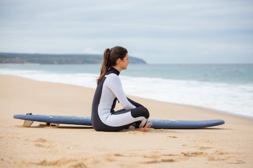 Woman Sitting on The Beach Beside a Surfboard