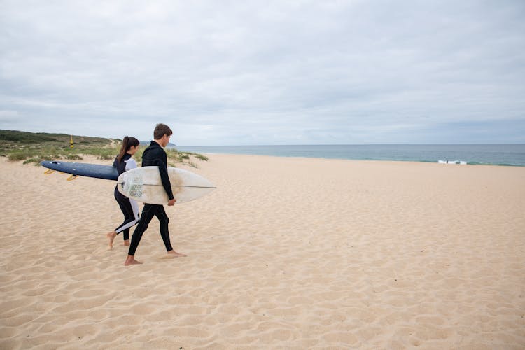 Man And Woman Holding Their Surfboards Walking Towards The Sea