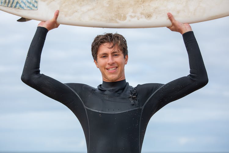 A Man In A Wetsuit Carrying Surfboard 