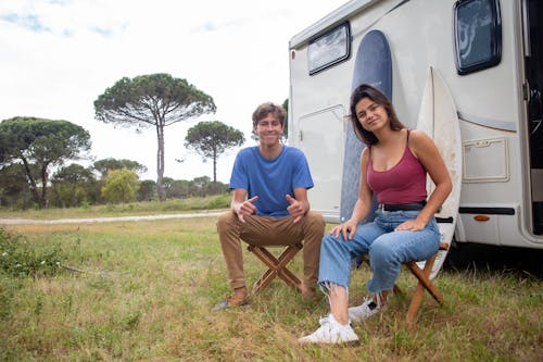 Young Man and Woman Sitting in front of a Campervan and Smiling 