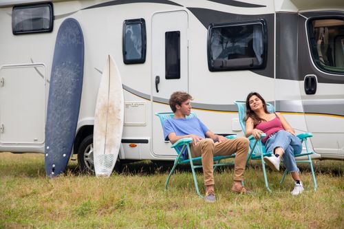 Free Couple relaxing by an RV with surfboards on a grass field, enjoying leisure time in Portugal. Stock Photo