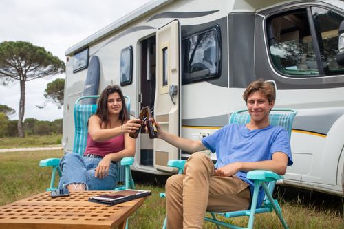 Free Happy couple clinking beer bottles outside camper during a relaxing vacation in Portugal. Stock Photo