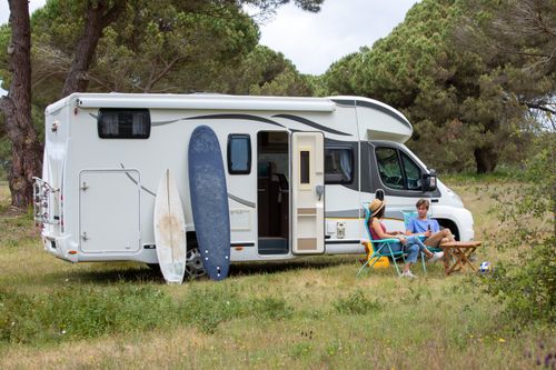 Free A couple relaxes outside their RV with surfboards at a scenic campsite in Portugal, enjoying a summer vacation. Stock Photo