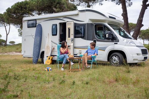 Free Young couple relaxing outside their RV with surfboards and guitar, enjoying a summer day in Portugal. Stock Photo