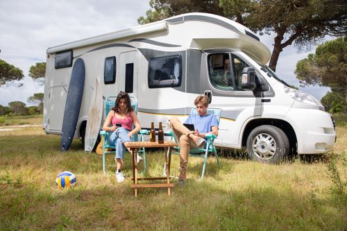 Free A couple enjoys a sunny day relaxing by their camper van in a picturesque outdoor setting in Portugal. Stock Photo
