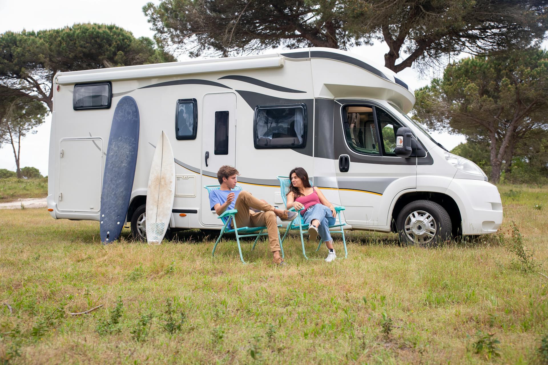 A young couple enjoys leisure time by their campervan in a sunny outdoor setting.