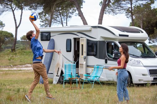 Free A young couple playing volleyball near their camper van on a sunny day in Portugal's scenic outdoors. Stock Photo