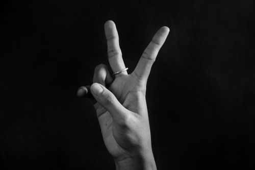 Free Hand making a peace sign gesture in a striking black and white photograph with a dark background. Stock Photo