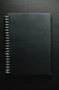 Vertical shot of a black spiral notebook against a dark background, perfect for mockups.