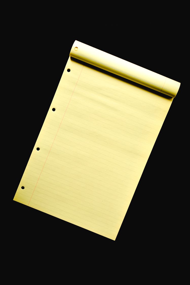 A Pad Of Yellow Paper Over Black Surface