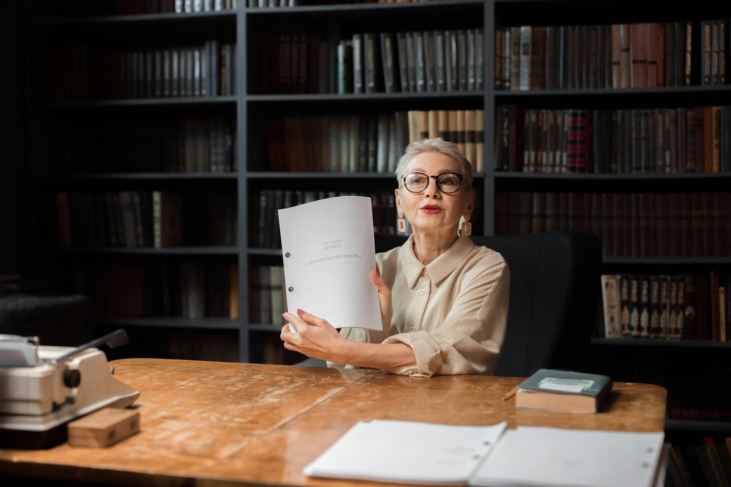 Senior woman with manuscript at a wooden desk in a library, showcasing documents.