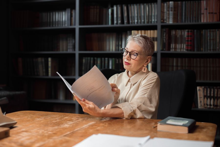 Writer reading a manuscript at a desk in front of a wall of bookshelves — photo by Ron Lach on Pexels