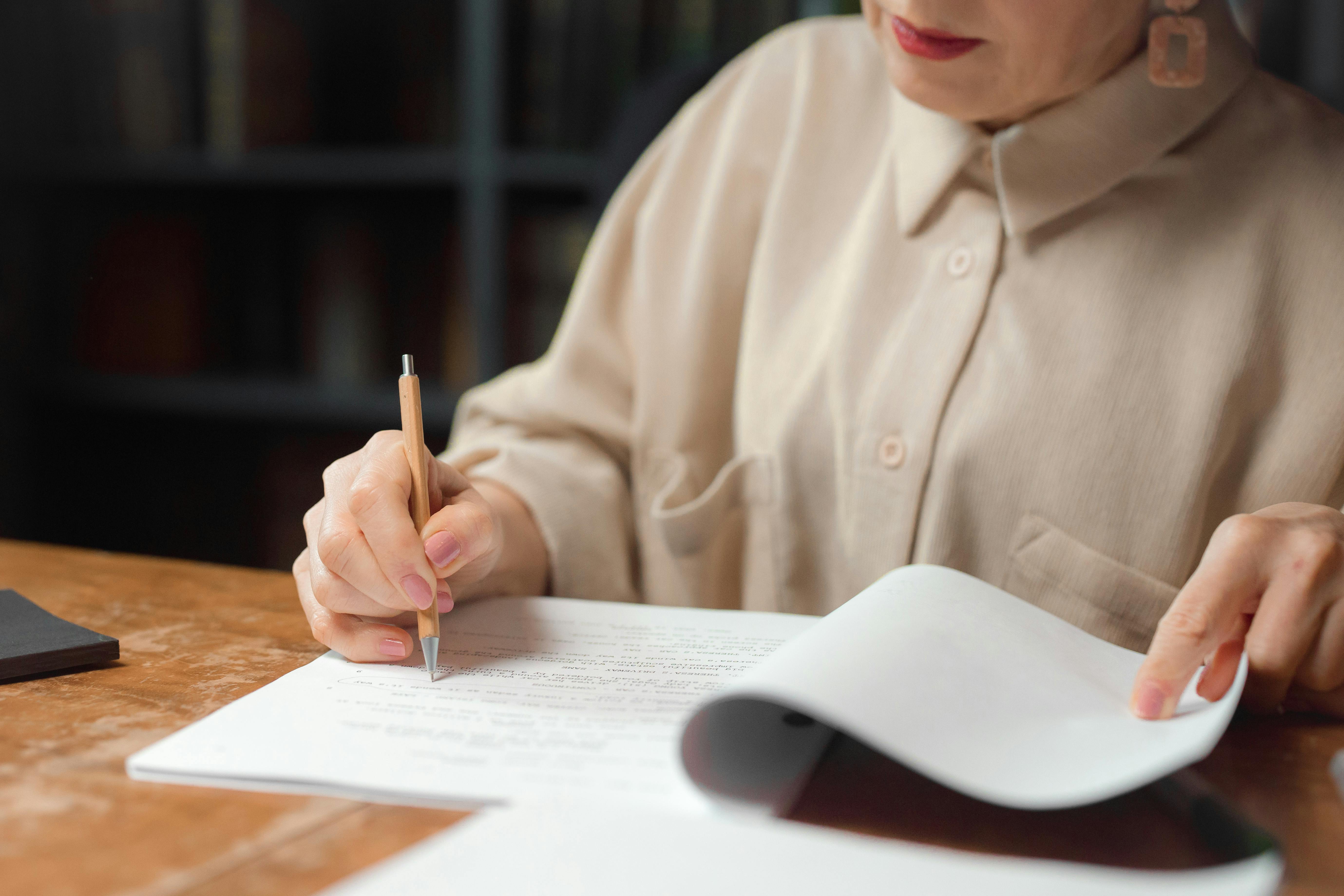 Person fills out paperwork with a pen while reviewing documents at a desk