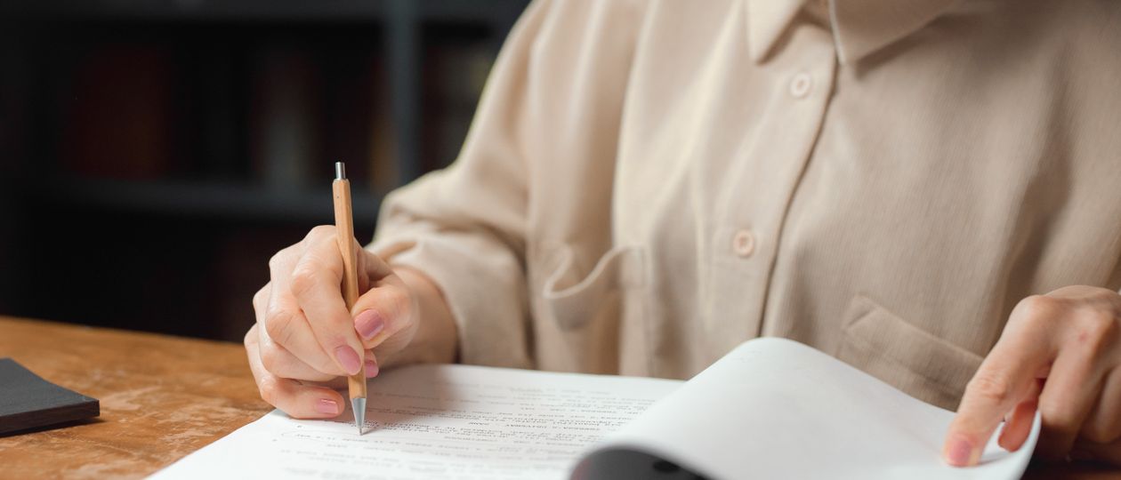 Persoon maakt aantekeningen bij papieren aan een houten tafel