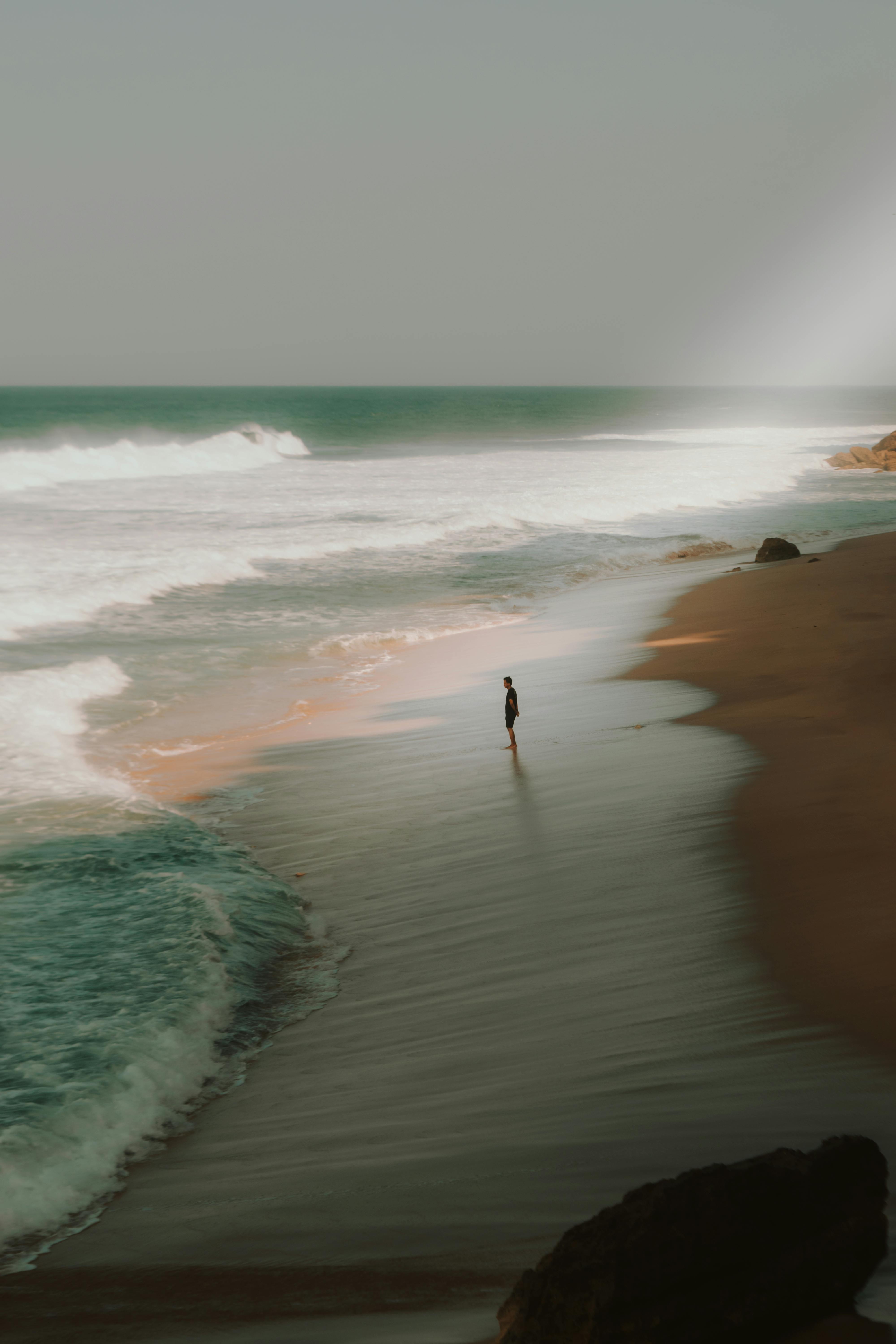 A peaceful beach with waves crashing and a solitary figure standing by the shore.