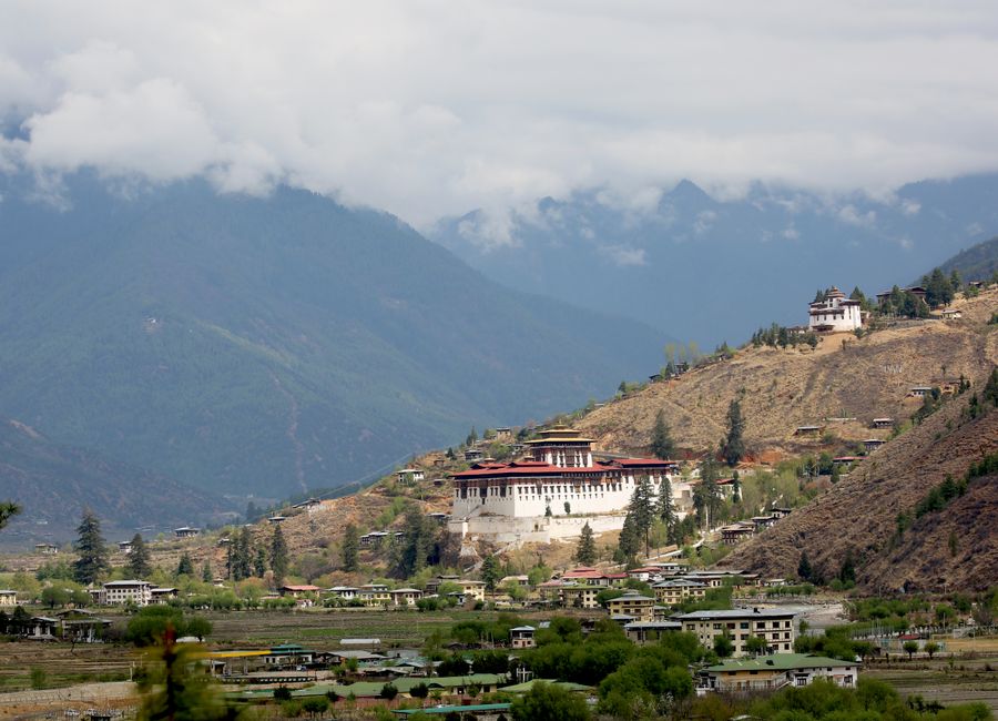 Scenic view of Paro Valley with Rinpung Dzong, surrounded by mountains and clouds in Bhutan.