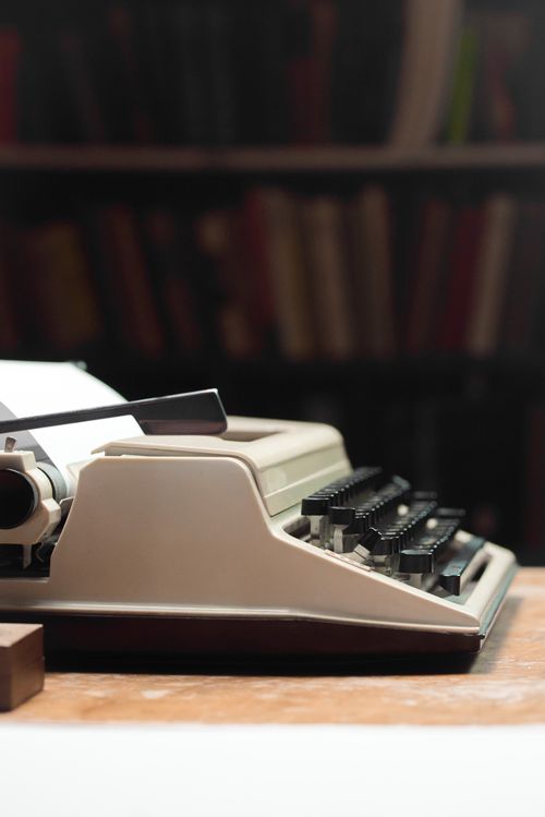 Free Close-up of a vintage typewriter on a wooden desk in a cozy library setting. Stock Photo