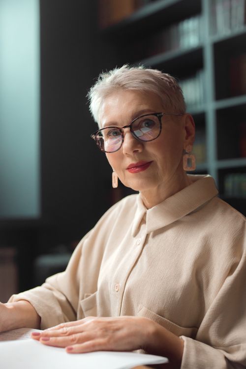 Free Portrait of a stylish senior woman with white hair and eyeglasses, sitting indoors. Stock Photo