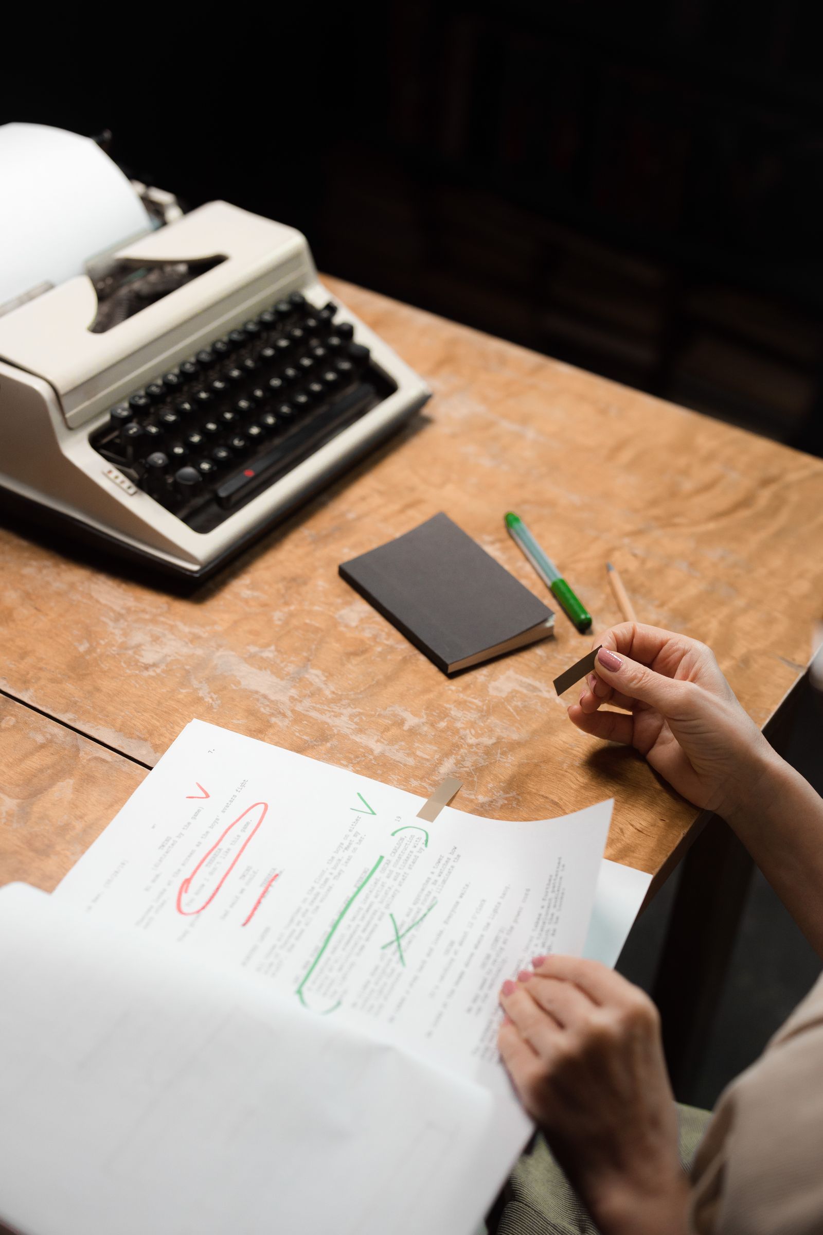 A person reviewing a paper document at a wooden desk beside a typewriter