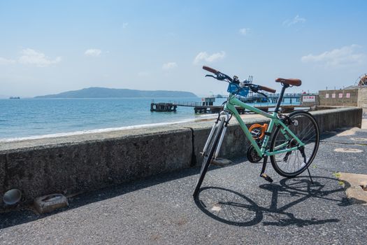 A scenic view of a bicycle parked by the sea in Fukuoka, Japan with a clear blue sky.