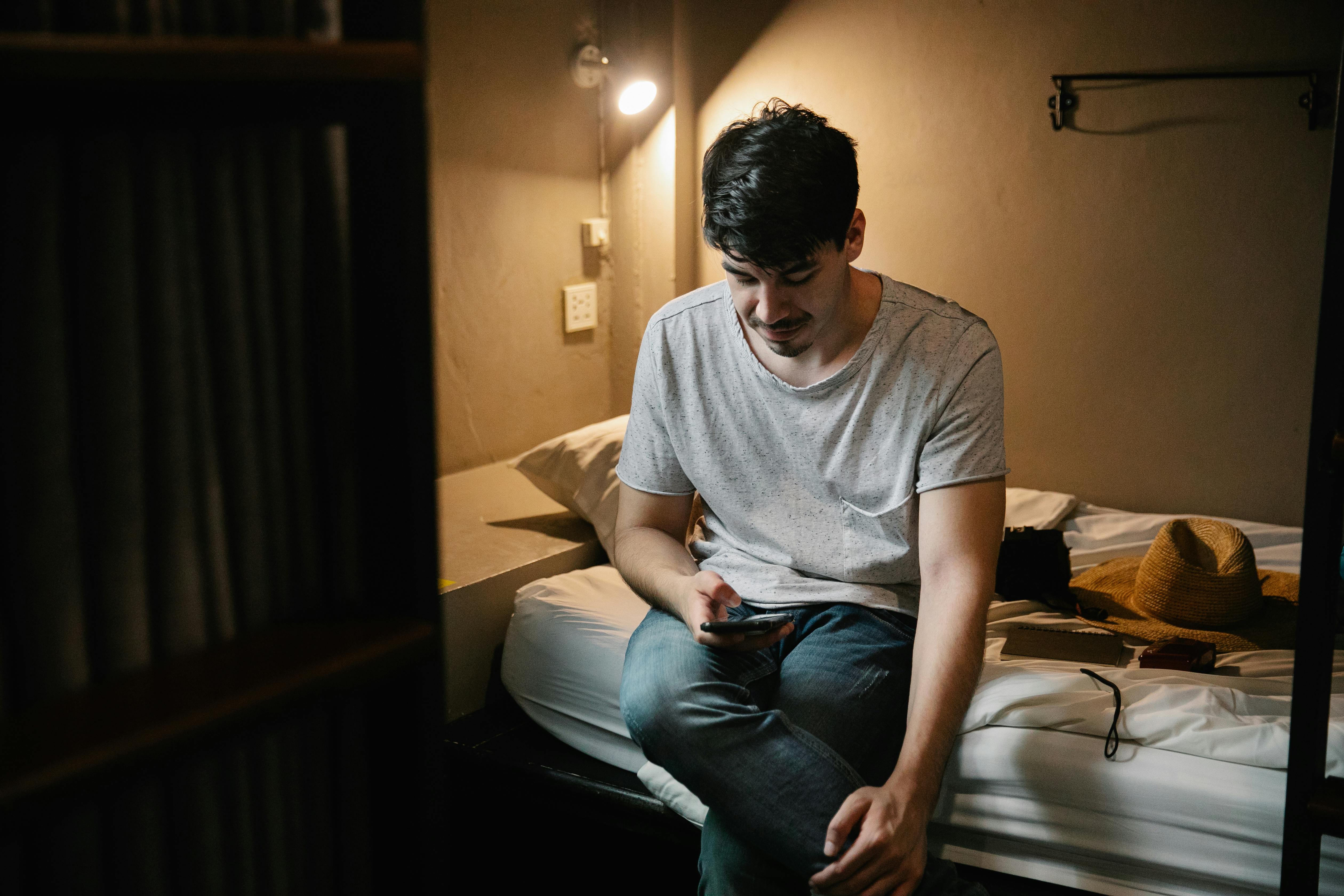 man sitting on bed and using smartphone