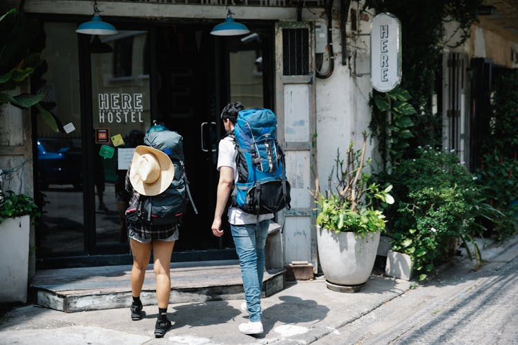 Unrecognizable Couple Of Travellers With Backpacks Entering Hotel