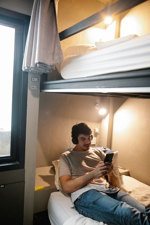 Free Adult male lounging on a bunk bed, wearing headphones and using smartphone. Cozy indoor setting. Stock Photo