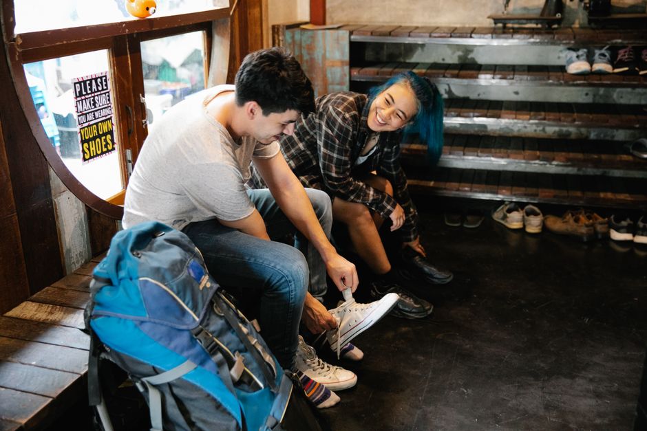 Side view of young multiethnic people sitting on wooden bench and changing shoes in cabin