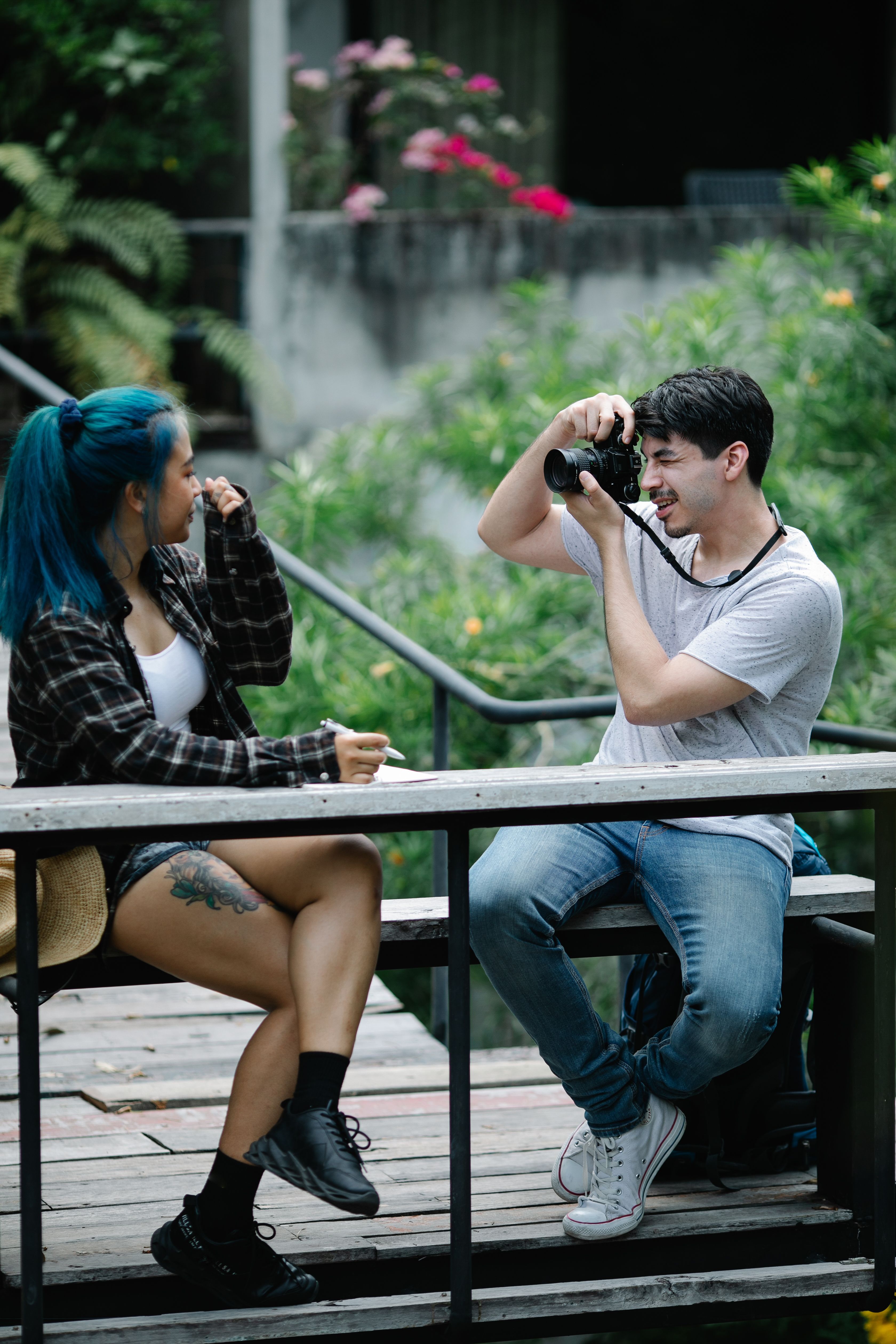 Two adults capturing natural moments outdoors with trees and flowers.