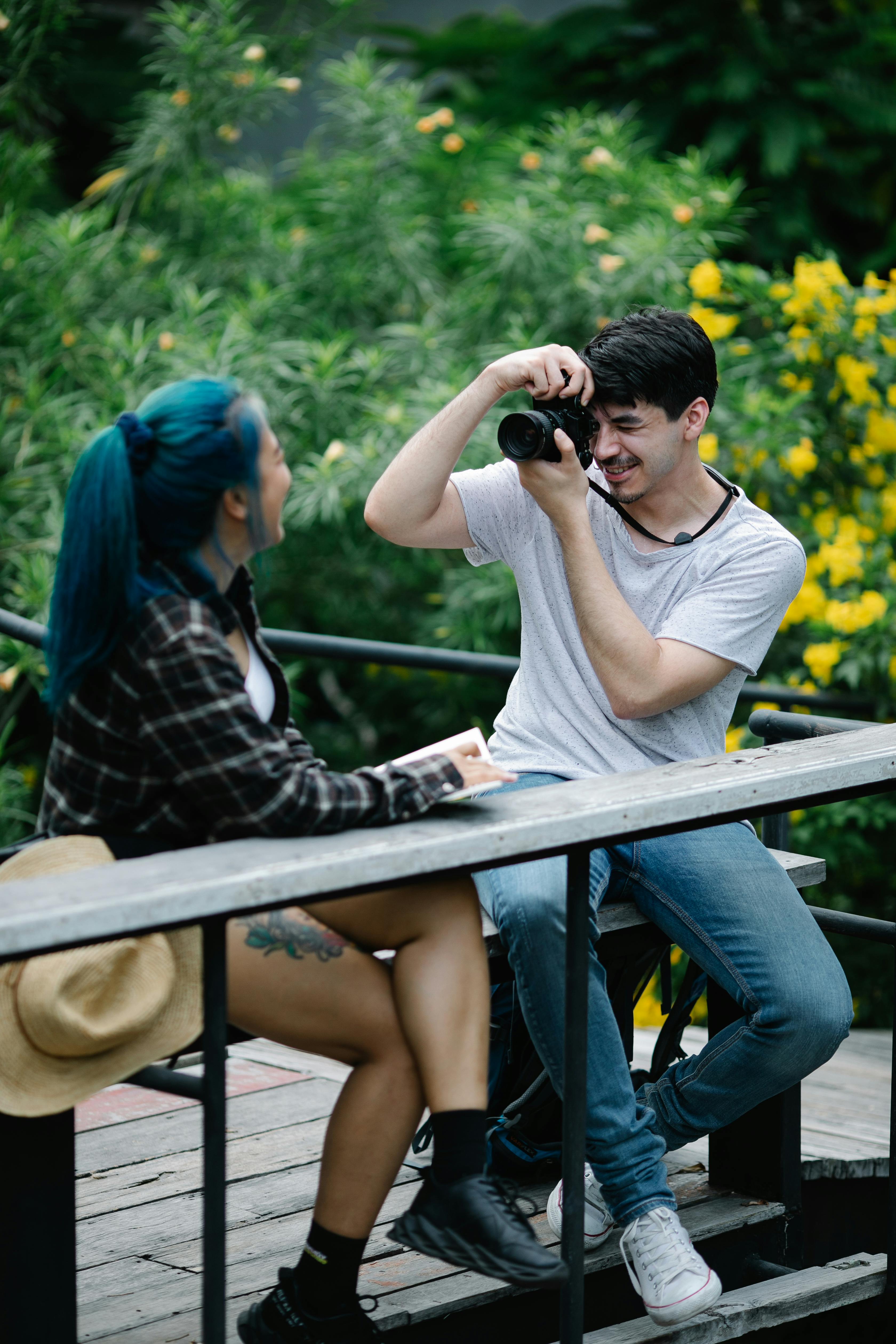 young man photographing girlfriend sitting on bench