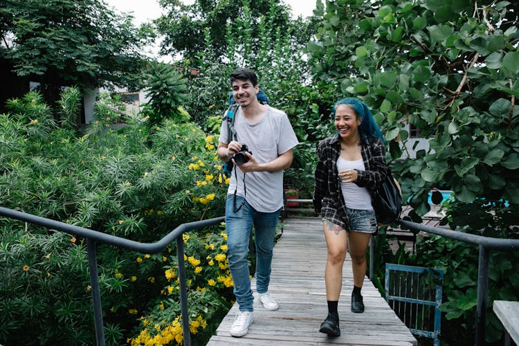 Cheerful Multiracial Friends Running In Footbridge In Summer Garden