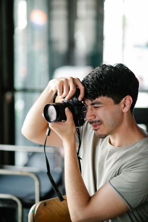 Free Side view of concentrated talented bearded male photographer taking picture on professional modern photo camera in light cafeteria near window Stock Photo