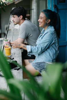 A cheerful couple enjoys drinks on a lush terrace, surrounded by greenery.