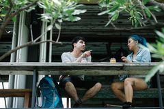 A couple enjoys drinks and conversation at an outdoor café table surrounded by greenery.